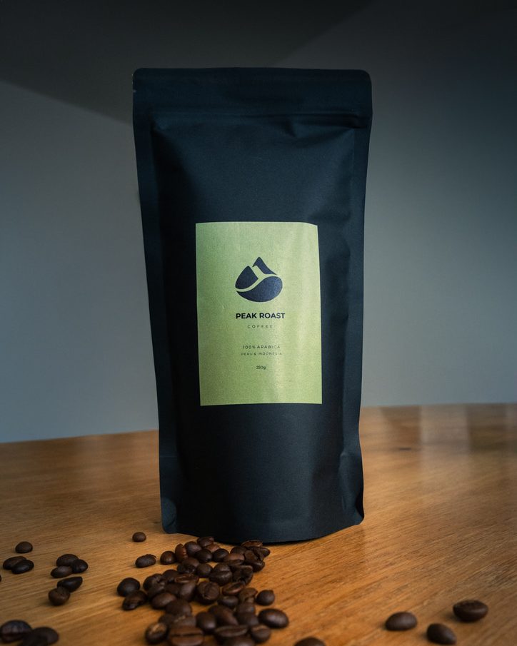 PEAK ROAST Packung auf einem Holztisch, davor Kaffeebohnen